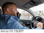 Side view man with a beard using mobile phone while driving car to work. Risky, reckless driver bad habits. Traffic safety rule violation lack of attention concept. Стоковое фото, фотограф Ирина Михайличенко / Фотобанк Лори