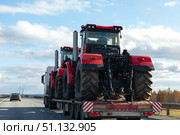 A tow truck transports two red farm tractors along a highway after work in field. Heavy-duty transport and agricultural machinery delivery concept. Logistics cargo transport. Стоковое фото, фотограф Ирина Михайличенко / Фотобанк Лори