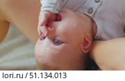 A little boy with blue eyes sucks his finger while lying in his mother's arms. Close-up. There is milk on the baby's cheek. The period of breastfeeding. Стоковое видео, видеограф Воловодов Владимир / Фотобанк Лори