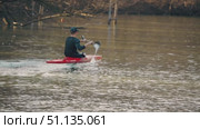 A person paddles a red kayak on calm waters, creating ripples as they navigate through serene surroundings. Trees in the background hint at a peaceful wilderness. Krasnodar, Russia, March 3, 2025. Редакционное видео, видеограф Воловодов Владимир / Фотобанк Лори