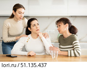 Sad woman sits silently in kitchen, adult girls sympathize and comfort her. Стоковое фото, фотограф Яков Филимонов / Фотобанк Лори