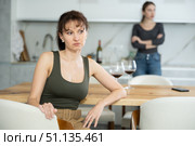 Upset middle-aged woman sitting at the kitchen table with her back to another lady quarreling to her. Стоковое фото, фотограф Яков Филимонов / Фотобанк Лори