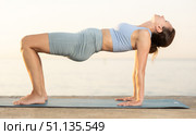 Portrait of caucasian experienced woman yoga teacher performs ardha chakrasana on seashore at sunset. Стоковое фото, фотограф Яков Филимонов / Фотобанк Лори