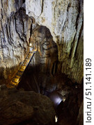 Dark cave view from inside with a lumen. Stalactites and stalagmites inside the stone grotto. Colorful stones in the cave. Lighting electricity beauty of the cave. (2019 год). Стоковое фото, фотограф Наталия Кирсанова / Фотобанк Лори