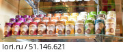 A bright display case with a variety of jars of instant flavored coffee. Glass jars with different flavors are neatly arranged on the shelves in several rows: Ecuador, Hazelnut, Tiramisu, Colombia, Chocolat, Cappuccino, Caramel, Vanilla, White Chocolate, Brazil, Date and others. Each jar has a colored lid that matches the flavor: purple, brown, yellow, green and white tones create a rainbow effect. The photo conveys the atmosphere of a coffee shop or a cozy coffee house, where customers can choose coffee to their taste. The photo emphasizes the variety of the assortment and the aesthetics of the display case design. (2015 год). Редакционное фото, фотограф Анна Кривицкая / Фотобанк Лори