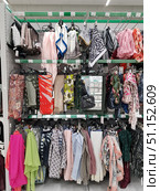 A rack with women's accessories in a store. Various shawls, scarves and stoles of different colors and patterns are neatly hung on hangers. Products made of lightweight fabrics, bright models with geometric, floral and abstract prints, as well as plain options in pastel and rich tones are visible. The assortment demonstrates a wide choice of fashionable accessories for every taste - from strict and classic to bright and creative. In the background, price tags and product labels are noticeable, emphasizing the store format. The photo conveys the atmosphere of the sales area and the variety of goods for customers. (2019 год). Редакционное фото, фотограф Анна Кривицкая / Фотобанк Лори