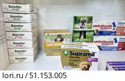 Veterinary pharmacy display cases with products for protecting animals from fleas, ticks and helminths. In the foreground are BlohNet Max packages in different dosages for dogs and cats. In the center are boxes of Profender, a product for helminths for cats. On the right are Drontal Plus packages for dogs, as well as popular Milbemax antihelminthic tablets for dogs of different sizes. Also visible in the foreground is Supramil, a product for helminths for puppies and dogs. All packages have a bright design with images of cats and dogs, as well as dosages. The photo is of good quality, with clearly legible names and markings. Suitable for use in catalogs of online pet stores, veterinary pharmacies, educational and advertising materials. Редакционное фото, фотограф Анна Кривицкая / Фотобанк Лори