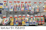 Store shelves with a wide range of watercolor paints. The display case features sets from different brands, including Erich Krause, Luch, Gamma and other manufacturers. The palettes are varied: classic round and rectangular trays, watercolors with pastel shades, as well as paints in original packages with cartoon characters. The number of colors varies from 6 to 18, there are sets with brushes and a palette. Each package has a bright design, aimed at both children and schoolchildren and aspiring artists. Above the products are price tags with promotional discounts. The image shows neatly laid out drawing supplies and is perfect for illustrating the range of stationery stores, online catalogs, educational projects and advertising materials. Редакционное фото, фотограф Анна Кривицкая / Фотобанк Лори