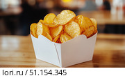 Crispy Potato Chips Served in a White Takeout Box on a Wooden Table in a Casual Dining Setting. Стоковое AI-изображение, AI-художник Юлия Гапеенко / Фотобанк Лори