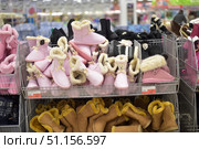 Shelves in a store with a large selection of winter house shoes. In the foreground are soft, warm ugg slippers with a fur lining. The top tier of the basket contains pink slippers with decorative elements in the form of a bear's face and bows, as well as black and dark models. The bottom tier contains classic brown fur ugg slippers. The products are made of soft materials that provide comfort and warmth in the cold season. The photo illustrates the assortment of the clothing and shoe store, the winter collection and the cozy style of house shoes. (2015 год). Редакционное фото, фотограф Анна Кривицкая / Фотобанк Лори