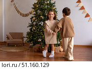 Happy little children, boy and girl holding hands, having fun and dancing near decorated Christmas tree in the morning. Merry Christmas and Happy New year winter holidays. High quality photo. Стоковое фото, фотограф Ирина Михайличенко / Фотобанк Лори