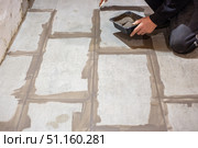 A worker applies grout between newly laid large floor tiles using a small container for the material. Стоковое фото, фотограф Коханова Наталья / Фотобанк Лори