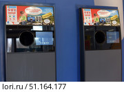 Two modern machines for accepting plastic bottles and aluminum cans, installed in a shopping center or supermarket. The devices are designed to return containers for subsequent processing and issuing a cash or bonus check to the buyer. At the top of the machines there are advertising posters in Finnish with information about the promotion and possible prizes, among which a gold bar and a boat are mentioned. In the center of the machine there is a round hole for accepting bottles, next to which there is a touch screen for selecting options and interacting with the user. The background of the wall is painted in bright blue, emphasizing the modern look of the equipment.The photo is perfect for topics related to waste recycling, environmental protection, plastic recycling, ecology, as well as for illustrations dedicated to supermarket infrastructure and automated container return systems. (2015 год). Редакционное фото, фотограф Анна Кривицкая / Фотобанк Лори
