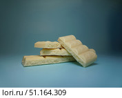 Кусочки белого шоколада, уложенные друг на друга на синем фоне. Пористая структура шоколада хорошо видна на изломах. Освещение мягкое, без резких теней. Стоковое фото, фотограф Анна Чижова / Фотобанк Лори
