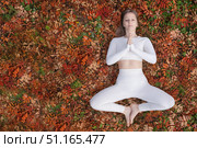 In peaceful outdoor setting during autumn, a woman performs a yoga pose on a vibrant carpet of colorful leaves. Dressed in white workout clothing, maintains meditative stance hands in prayer position. Стоковое фото, фотограф Владимир Разгуляев / Фотобанк Лори