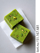 Green pistachio barfi pieces garnished with chopped nuts, resting on parchment paper, highlighting traditional indian sweet delicacy. Стоковое AI-изображение, AI-художник Юрий Поздников / Фотобанк Лори