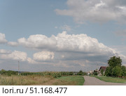 Summer clear sunny village landscape with white cumulus clouds, road and houses along street. Стоковое фото, фотограф irisff / Фотобанк Лори