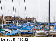 Whitstable Harbour dinghies on shingle beach, masts and boatyard sheds. Whitstable, UK, 2 July 2024. Редакционное фото, фотограф Zydrius Tartenis / Фотобанк Лори