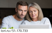 A middle-aged woman and a younger man are sitting together, attentively looking at a laptop screen. Their expressions suggest they are focused or engaged in reading something important. This cozy, intimate setting reflects family connection and intergenerational bonding, a common theme during significant Russian holidays such as Defender of the Fatherland Day, International Women's Day, or even New Year planning. The image represents togetherness, support, and the quiet moments of preparation and reflection often associated with national celebrations and family gatherings in Russia. Стоковое AI-изображение, AI-художник Ксения Чунаева / Фотобанк Лори