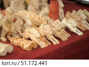 Hand-made wooden figurines depicting various animals and characters. In the foreground are carved hares and mice in various stages of processing - from rough blanks to detailed elaboration of muzzles and ears. On the left is a noticeable human figurine, and in the background - a bear, a hedgehog and other characters. All figurines are made of natural wood without painting, which emphasizes the texture and warmth of the natural material. The atmosphere of the photo conveys the spirit of folk art, crafts and traditional wood carving. Стоковое фото, фотограф Анна Кривицкая / Фотобанк Лори