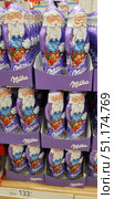 Shop windows with chocolate figurines in the form of Santa Claus from the Milka brand. The figurines are wrapped in purple foil with an image of Santa holding a gift and a teddy bear. The product is made of Alpine milk chocolate, as indicated by the inscription on the packaging "Alpenmilch Alpine Milk Lait". The price is visible in the foreground - 133.51 rubles per unit. The bright and festive packaging emphasizes the New Year's mood, and the composition demonstrates a whole display of goods ready for purchase. The photo is perfect for the theme of New Year's goods, holiday chocolate, Christmas sales and marketing. (2018 год). Редакционное фото, фотограф Анна Кривицкая / Фотобанк Лори