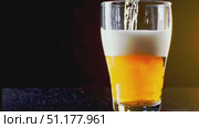 Medium close-up of a straight-sided pint filled with light-amber lager; dense white foam against a cool blue/black background. 4K MP4, no people. Стоковое AI-видео, аниматор Владислав Войтов / Фотобанк Лори
