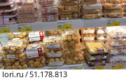 A supermarket display case with a large selection of confectionery products in plastic packaging. The shelves are lined with sets of cakes: profiteroles, eclairs with cream, rolls and cakes. The sweets are neatly packed in transparent containers, which allows the buyer to examine their appearance. The price tags under the display case indicate the cost in rubles. Whipped meringues are visible in the background, as well as various desserts in portioned boxes. The atmosphere of the photo conveys a sense of abundance and choice in the baking and confectionery department. (2015 год). Редакционное фото, фотограф Анна Кривицкая / Фотобанк Лори