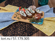 Закуски на деревянной доске, включая брускетты с сыром, прошутто и клубнику, на сервированном столе. Стоковое фото, фотограф Кирилл Сиротюк / Фотобанк Лори