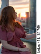 Woman in a burgundy dress stands on a rooftop at sunset, with modern skyscrapers of Moscow City in the background. Стоковое фото, фотограф Софья Соломонова / Фотобанк Лори