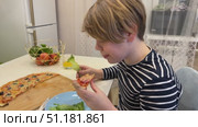 The young boy is munching on pizza in the kitchen, his eyes bright with excitement as he takes another big bite. Стоковое видео, видеограф Ирина Старикова / Фотобанк Лори