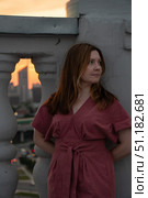 Woman in a rose dress leans against a rooftop balustrade at sunset with a blurred city skyline in the background. Стоковое фото, фотограф Софья Соломонова / Фотобанк Лори