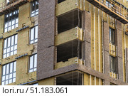 Monolithic concrete frame of apartment building under construction with partially attached facade cladding blocks. Energy efficiency. Installation of external wall thermal insulation with rock wool. Стоковое фото, фотограф Данила Большаков / Фотобанк Лори