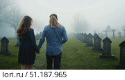 A couple walks together through a misty cemetery, surrounded by tombstones on a chilly evening in late autumn. Стоковое AI-видео, аниматор Данила Большаков / Фотобанк Лори