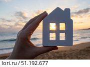 Hand holding white model house against beautiful sunset over the sea, symbolizing the dream of owning a seaside property. Стоковое фото, фотограф Данил Руденко / Фотобанк Лори