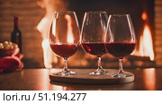Three glasses of wine are placed on table next to crackling fireplace. The soft glow of the flames illuminates the scene, creating a cozy and inviting ambiance. Стоковое AI-видео, аниматор Данила Большаков / Фотобанк Лори