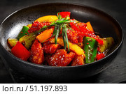Sweet sour pork with colorful peppers, mixed vegetables served in a black bowl on dark concrete background. Traditional Chinese dish. Close-up. The meat pieces in a brown sauce glaze. Sichuan cuisine. Стоковое AI-изображение, AI-художник Марина Демидюк / Фотобанк Лори