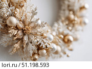 Delicate wreath of golden Christmas decorations hangs on the white wall. Magic and joy festive celebrations during the winter season. Elegant gold and silver Ornaments beautifully decorated setting. Стоковое фото, фотограф Марина Демидюк / Фотобанк Лори