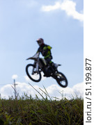 Magnitogorsk, Russian Federation - August 23, 2025: Male motocross rider in vibrant gear jumps over grassy terrain during enduro competition, showcasing thrilling action and skillful maneuvering. Редакционное фото, фотограф Ирина Ручушкина / Фотобанк Лори