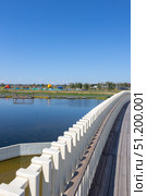 Magnitogorsk, Russian Federation - August 24, 2025: Scenic urban resort attraction featuring a wooden walkway beside a tranquil lake, colorful playgrounds in the background, ideal for family recreation and leisure activities. Редакционное фото, фотограф Ирина Ручушкина / Фотобанк Лори
