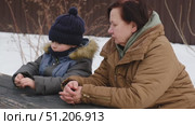 Grandmother swinging a child at the winter park or backyard. Grandma and grandchild sitting on swing. Senior 60s Granny pushing a kid boy on the rope seesaw. Old woman and little boy at the playground. Стоковое видео, видеограф Марина Демидюк / Фотобанк Лори