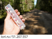 The traveler took the necessary medicines with him on a road trip in a weekly pillbox. Hand holding weekly pill organizer in front of forest path. Стоковое фото, фотограф Дмитрий Цветков / Фотобанк Лори