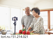 Elderly asian couple cooking together and filming in a modern kitchen setting. Стоковое AI-изображение, AI-художник Евгения Пархоменко / Фотобанк Лори