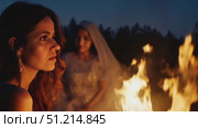 A woman stands thoughtfully beside a bonfire surrounded by trees, lost in her thoughts during a tranquil summer night gathering. Стоковое AI-видео, аниматор Данила Большаков / Фотобанк Лори