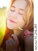 Young woman enjoying a warm sunny day while holding a flower in a blooming meadow. Стоковое фото, фотограф Кривошеина Елена Леонидовна / Фотобанк Лори