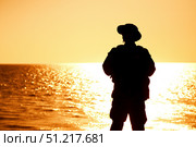 Silhouette of a soldier in boonie hat standing on the shoreline at sunset. Oleg Zabielin / Stocktrek Images/TASS. Стоковое фото, агентство ТАСС / Фотобанк Лори