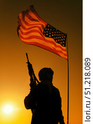 Silhouette of a U.S. soldier with assault rifle, standing under American flag, with sunset sky. Oleg Zabielin / Stocktrek Images/TASS. Стоковое фото, агентство ТАСС / Фотобанк Лори