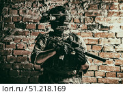 Special forces fighter standing against a brick wall, armed with thermal imaging device on helmet and submachine gun. Стоковое фото, агентство ТАСС / Фотобанк Лори