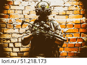 Special forces fighter standing against a brick wall, armed with thermal imaging device on helmet and submachine gun. Стоковое фото, агентство ТАСС / Фотобанк Лори