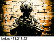 Special forces fighter standing against a brick wall, armed with thermal imaging device on helmet and submachine gun. Стоковое фото, агентство ТАСС / Фотобанк Лори