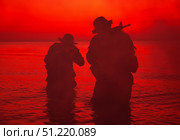 Silhouette of two soldiers wading the shoreline, sneaking in the darkness with assault rifles drawn. Oleg Zabielin / Stocktrek Images/TASS. Стоковое фото, агентство ТАСС / Фотобанк Лори